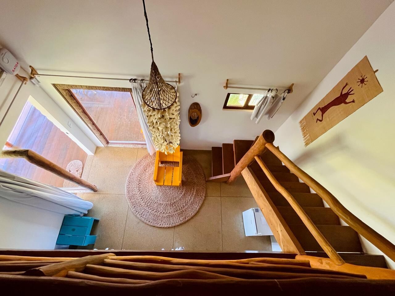 Una habitació àmplia amb una escala de fusta, una catifa teixida i un llum penjant.