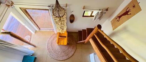 Una habitació àmplia amb una escala de fusta, una catifa teixida i un llum penjant.