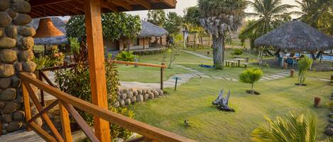 A resort with thatched-roof huts, a wooden deck, and a well-maintained garden with palm trees and a stone wall.