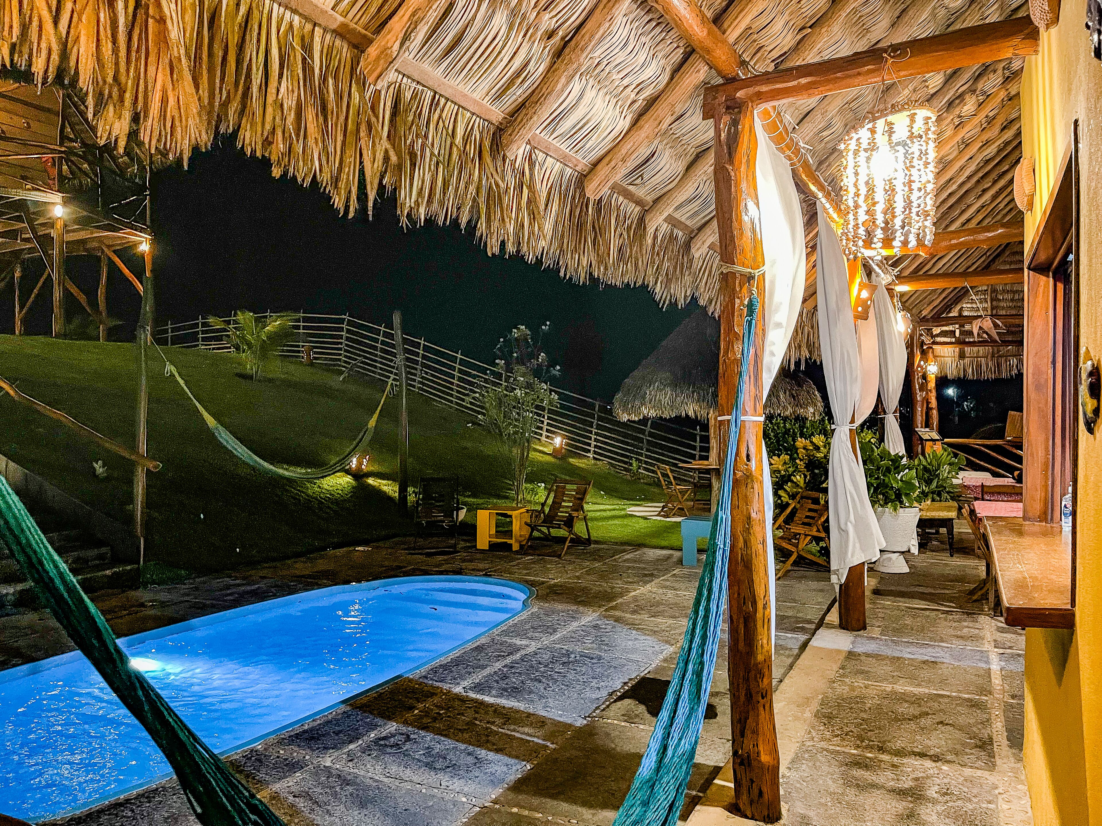 A thatched-roof outdoor area with a pool, seating, and a wooden structure.