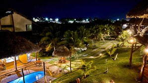A nighttime view of a resort with a swimming pool, thatched-roof structures, and well-lit pathways. - Pousada Theodora (Luis Correia)
