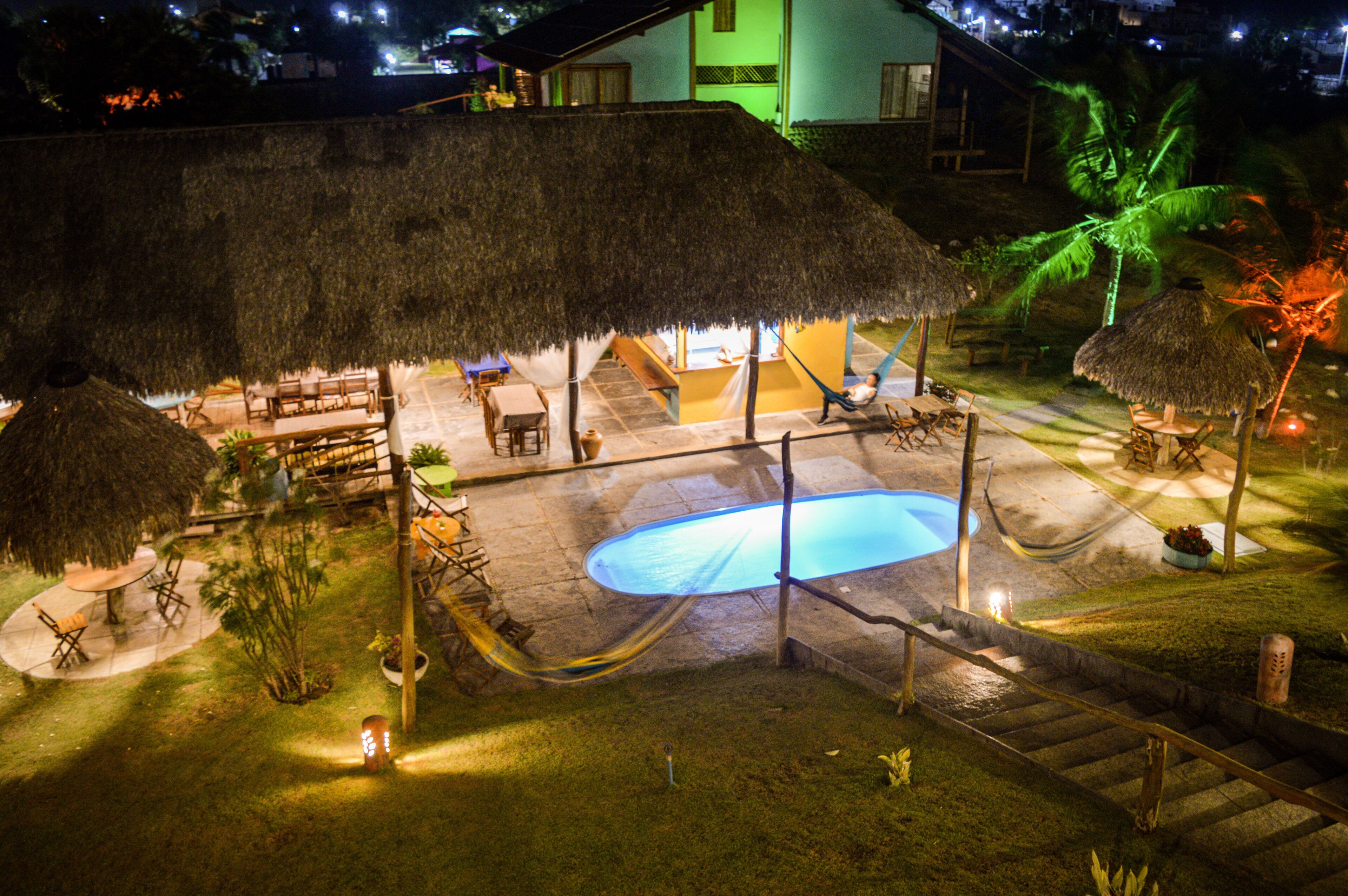 A thatched-roof outdoor area with a pool, seating, and a staircase leading up to a building.