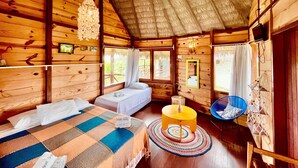 A wooden cabin room with a bed, a round yellow table, a blue chair, and a thatched roof. - Pousada Theodora (Luis Correia)