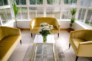 A room with two yellow armchairs, a glass coffee table, and a vase of white flowers.