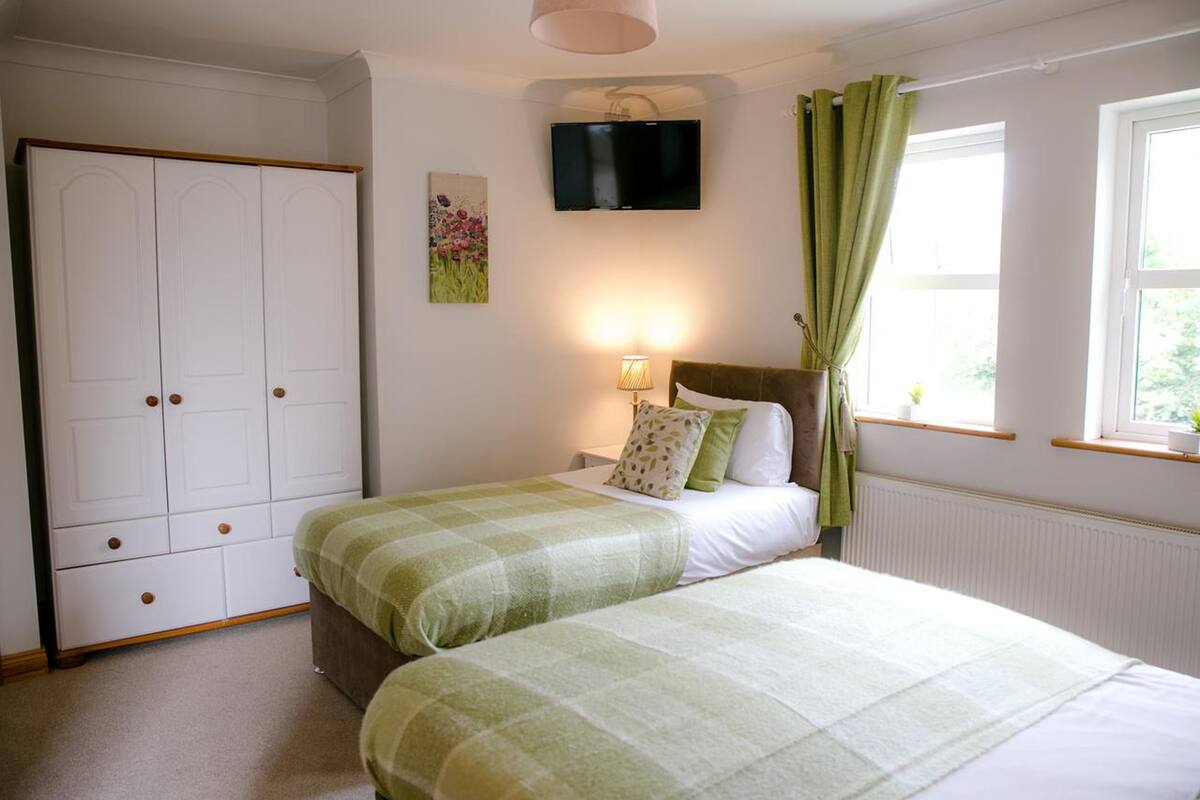 Een slaapkamer met twee bedden, een kledingkast, een televisie en een raam met gordijnen.