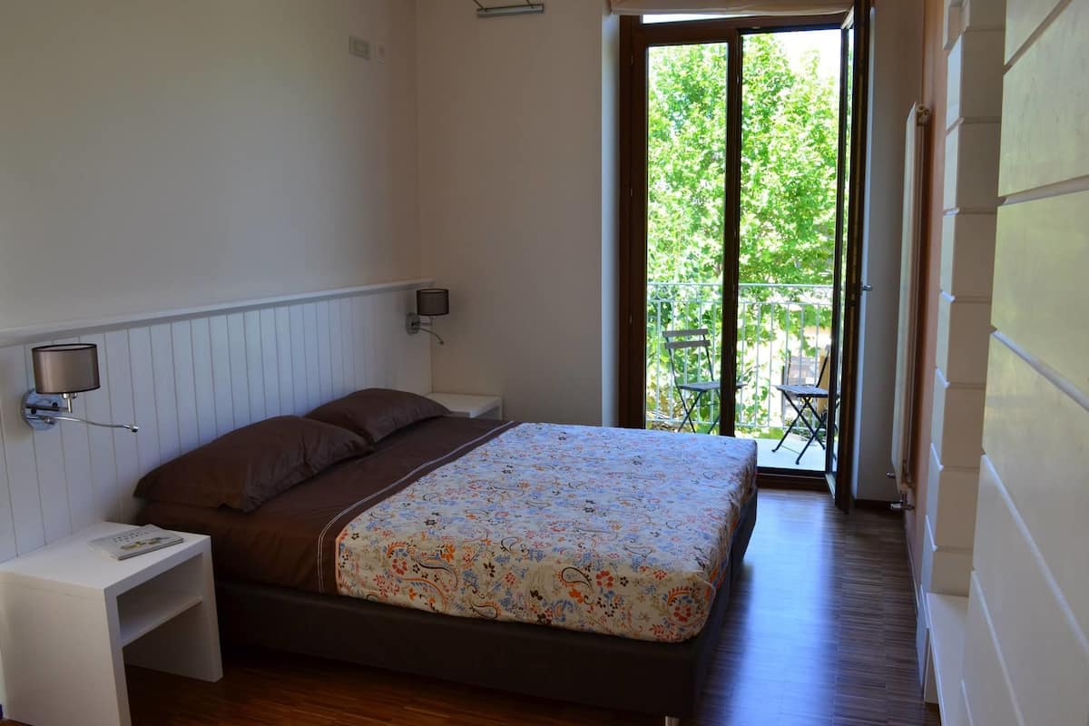 Un dormitorio con cama, mesita de noche, lámpara de pared y puerta al balcón.
