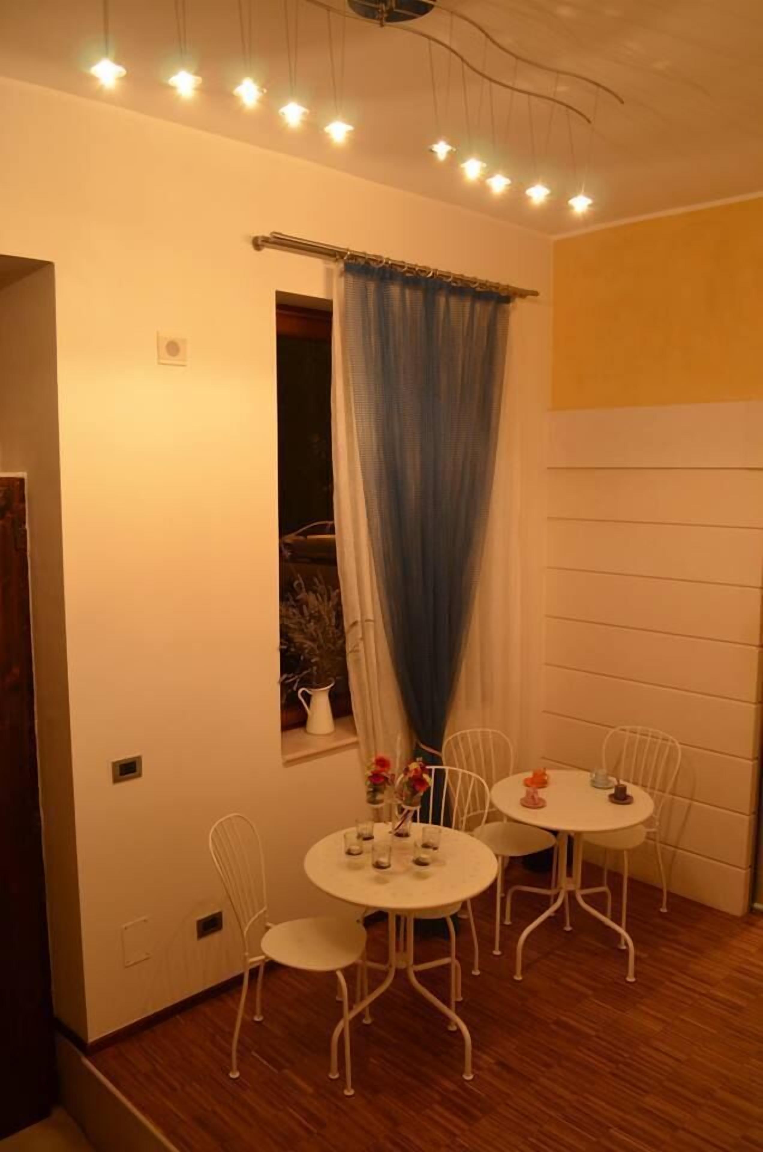 A small dining area with a round table and four chairs, a window with a curtain, and a ceiling light fixture.