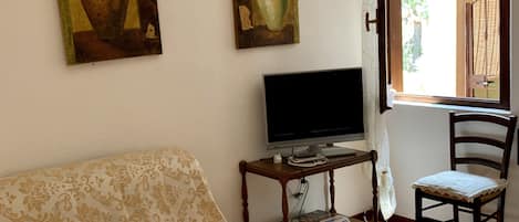 A living room with a sofa, a television, a chair, and two paintings on the wall.