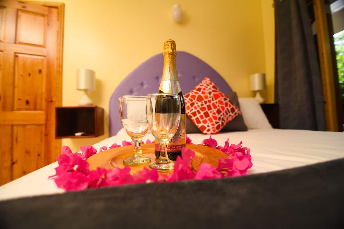 Una cama con una botella de champán, dos copas y pétalos de flores rosados.