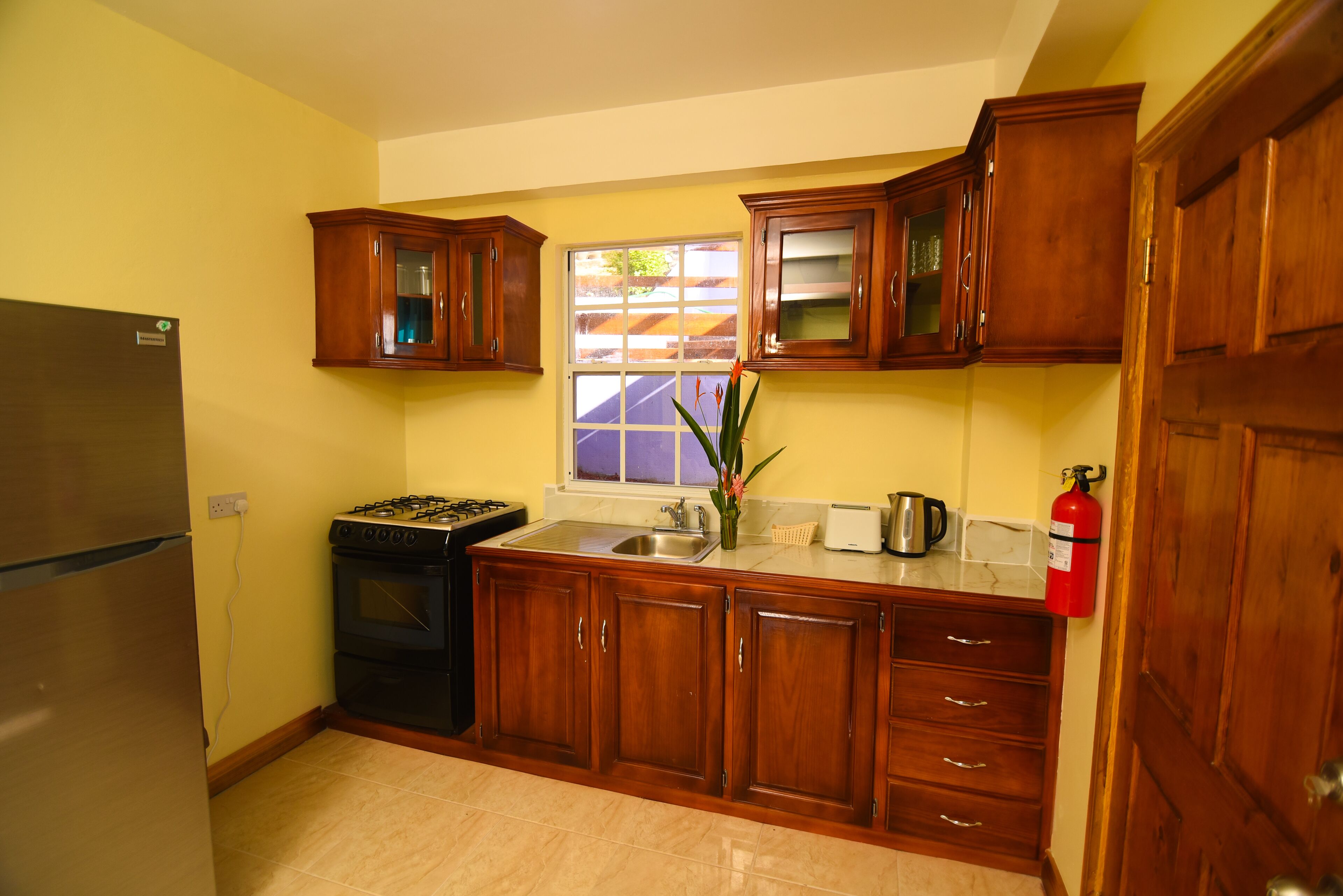 Una cocina con armarios de madera, un refrigerador de acero inoxidable, una estufa a gas y una ventana con vista a la calle.