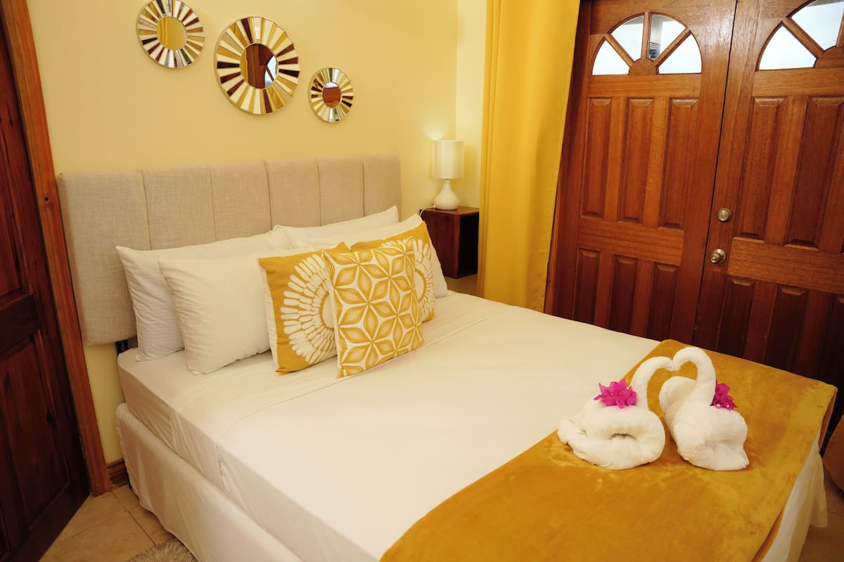 Una cama bien tendida con almohadas blancas y estampadas, una puerta de madera y una pared con espejos decorativos.