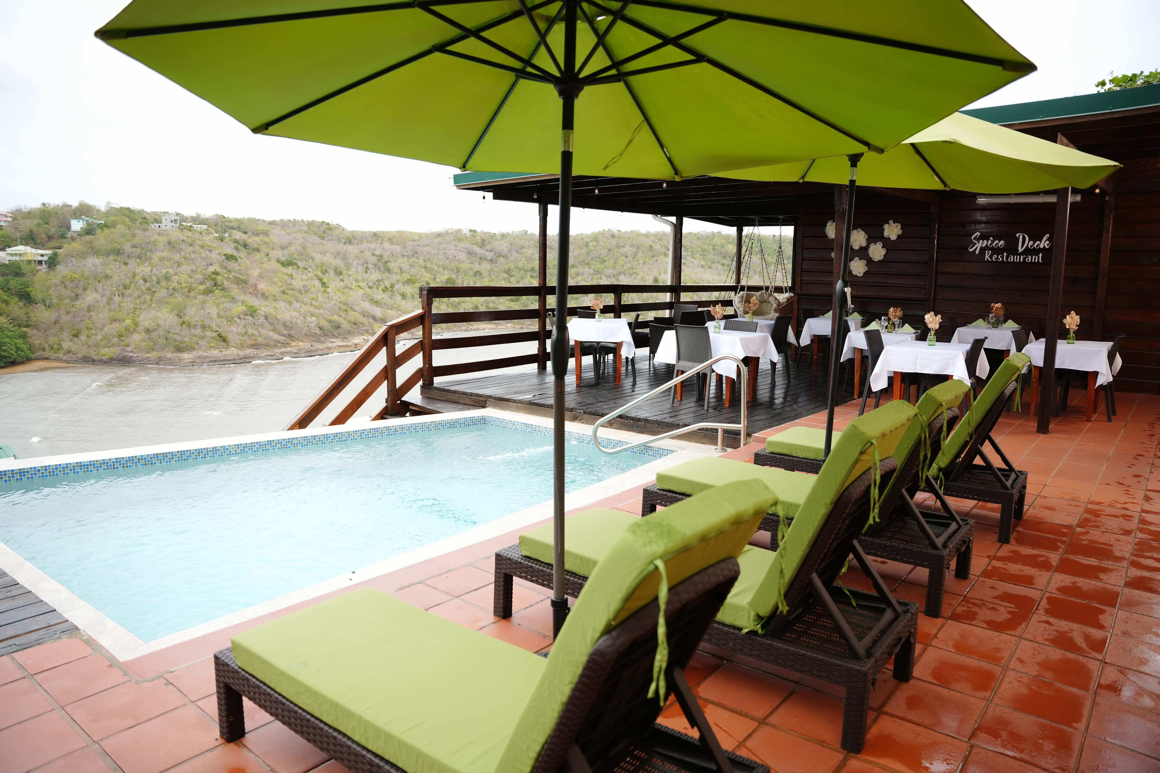 A poolside area with lounge chairs and umbrellas, a pool, and a restaurant named "Spice Deck Restaurant" with outdoor seating.