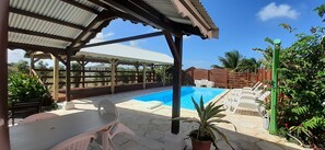 A covered outdoor area with a pool, lounge chairs, and a table.