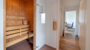 A wooden sauna room with benches and a door leading to a dining area. - Reede Hus Alfonso (Borkum)