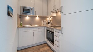 A compact kitchen with white cabinets, a microwave, a coffee maker, and a sink. - Reede Hus Alfonso (Borkum)