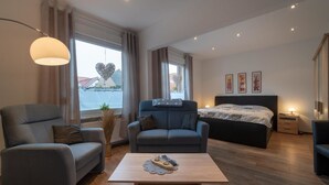 A modern bedroom with a bed, two sofas, a coffee table, and a large window with curtains. - Reede Hus Alfonso (Borkum)