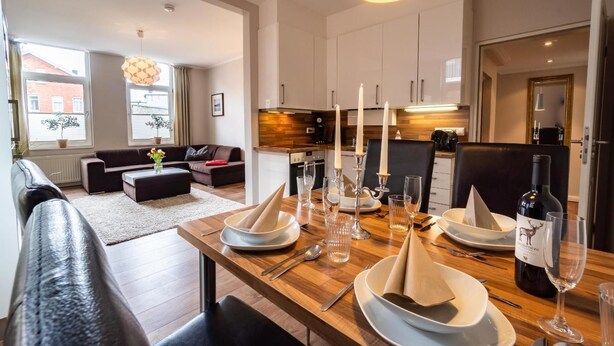 A modern living room with a sofa, a dining table set with plates, glasses, and a bottle of wine. - Altstadtvilla Wohnung Hochpaterre (Borkum)