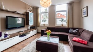 A modern living room with a flat-screen TV, a brown sofa, a glass coffee table, and a decorative pendant light. - Altstadtvilla Wohnung Hochpaterre (Borkum)