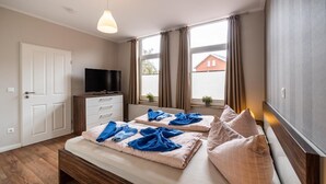 A bedroom with two beds, a TV, a dresser, and a window with curtains. - Altstadtvilla Wohnung Hochpaterre (Borkum)