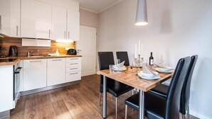 A modern kitchen with white cabinets, a wooden countertop, and a dining area with a wooden table set for four. - Altstadtvilla Wohnung Hochpaterre (Borkum)