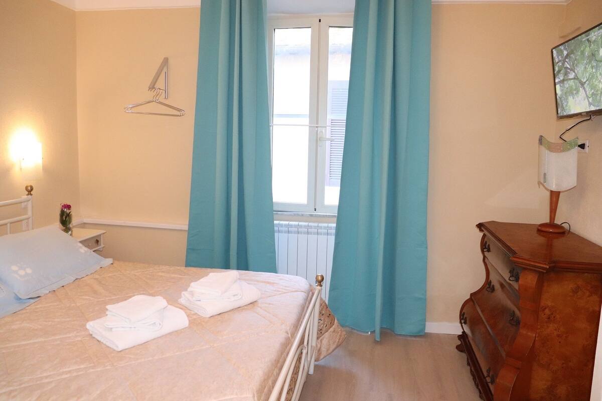 Une chambre à coucher comprenant un lit, une commode, un portant à vêtements et une fenêtre avec des rideaux.