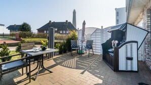 En udendørs terrasse med et bord, stole, grill og et hvidt hegn.