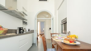 A modern kitchen with white cabinets, a dining table set with breakfast, and an open doorway leading to another room. - Elegant and comfortable apartment near the Duomo. The perfect location. (Firenze)