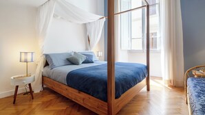 A four-poster bed with a canopy, a bedside table with a lamp, and a view of the outside through a window. - Elegant and comfortable apartment near the Duomo. The perfect location. (Firenze)