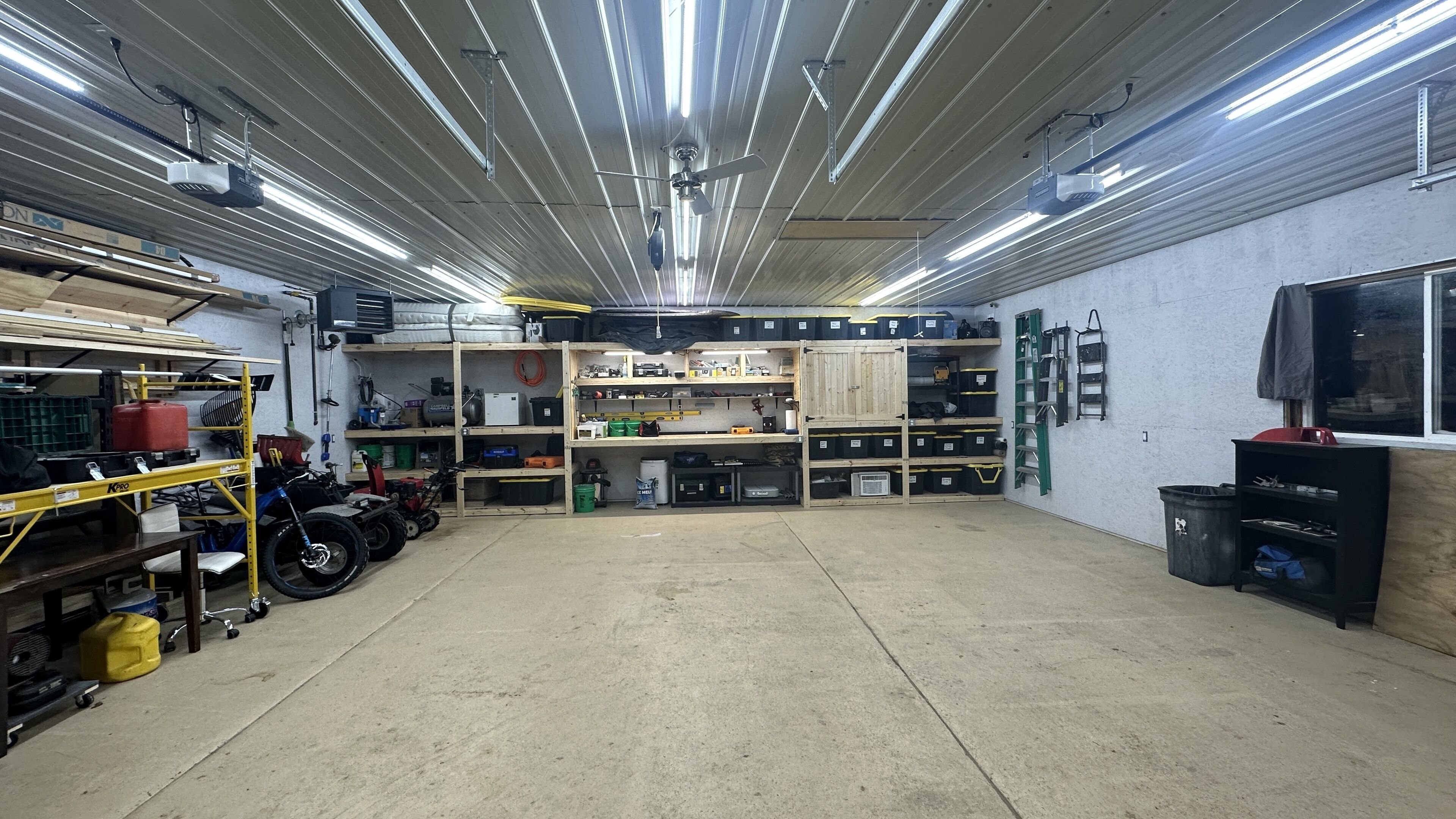 Un garage spacieux doté de hauts plafonds, d’un éclairage fluorescent et d’étagères de rangement bien organisées.