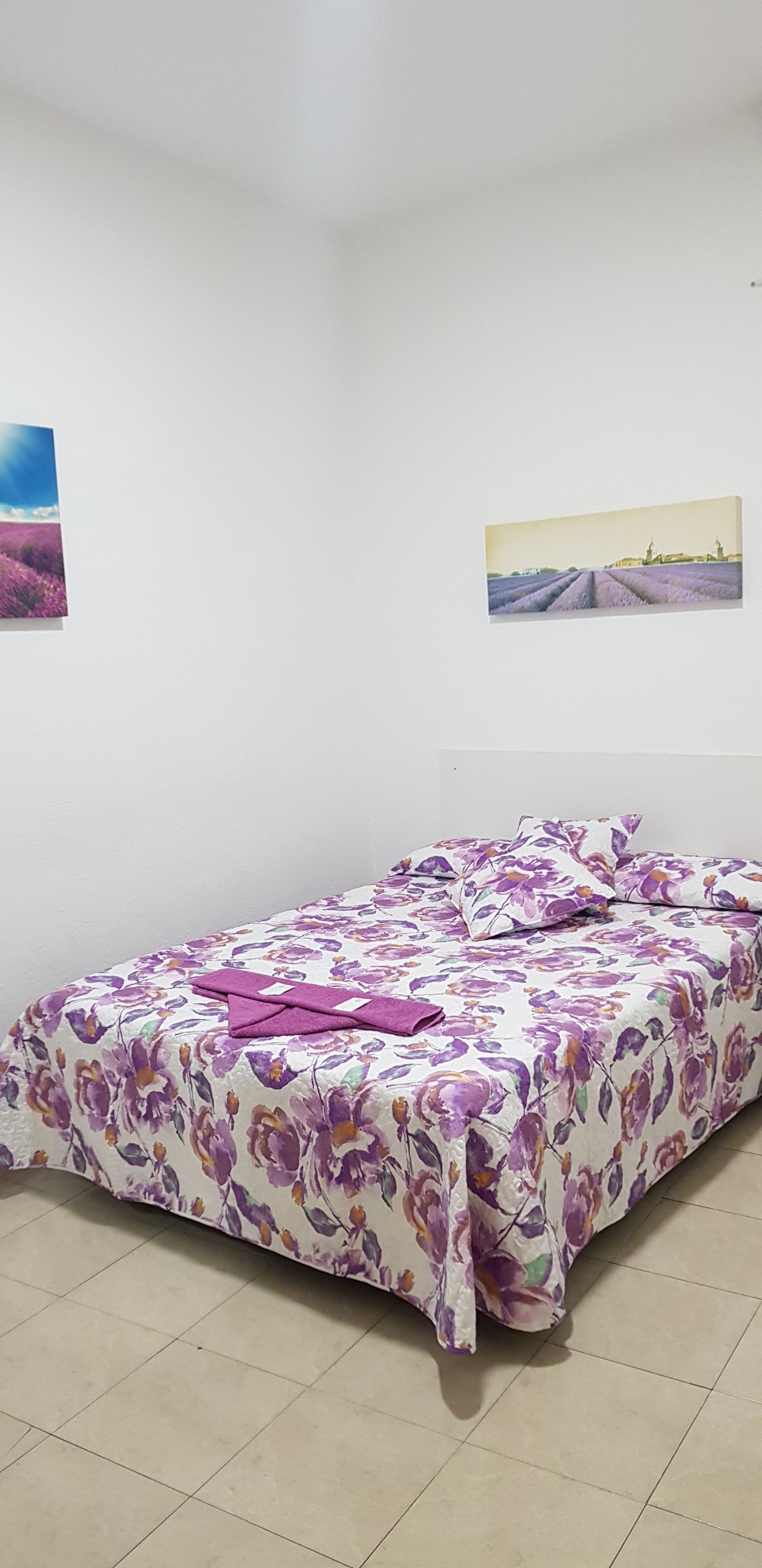 A bedroom with a floral bedspread, a neatly made bed with pillows, and two framed pictures on the wall.