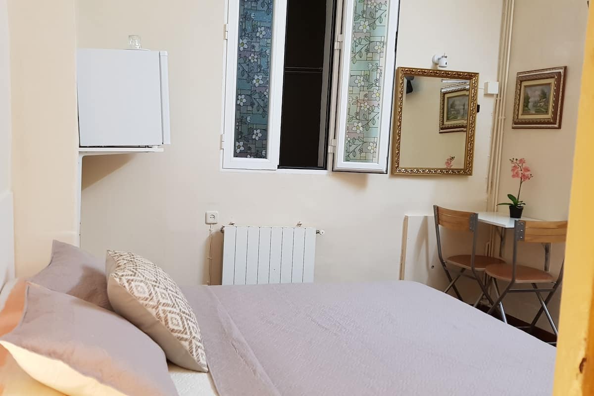 Une chambre à coucher comprenant un lit, un bureau, une chaise, un radiateur et une fenêtre donnant sur l’extérieur.