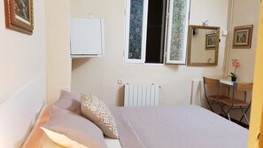 A bedroom with a bed, a desk, a chair, a radiator, and a window with a view of the outside. - Hostal Loyola - Hostel (Madrid)