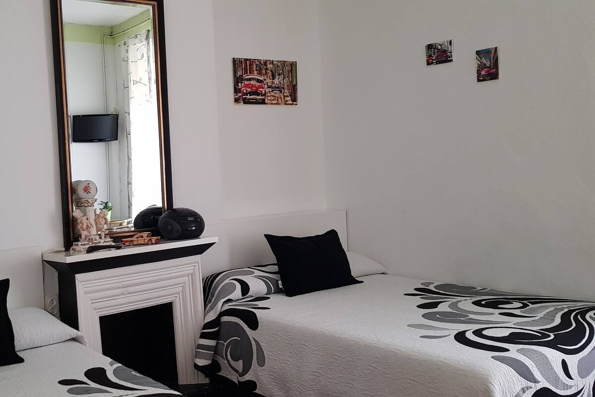 Une chambre avec deux lits, une cheminée, un miroir et des œuvres d’art accrochées aux murs.