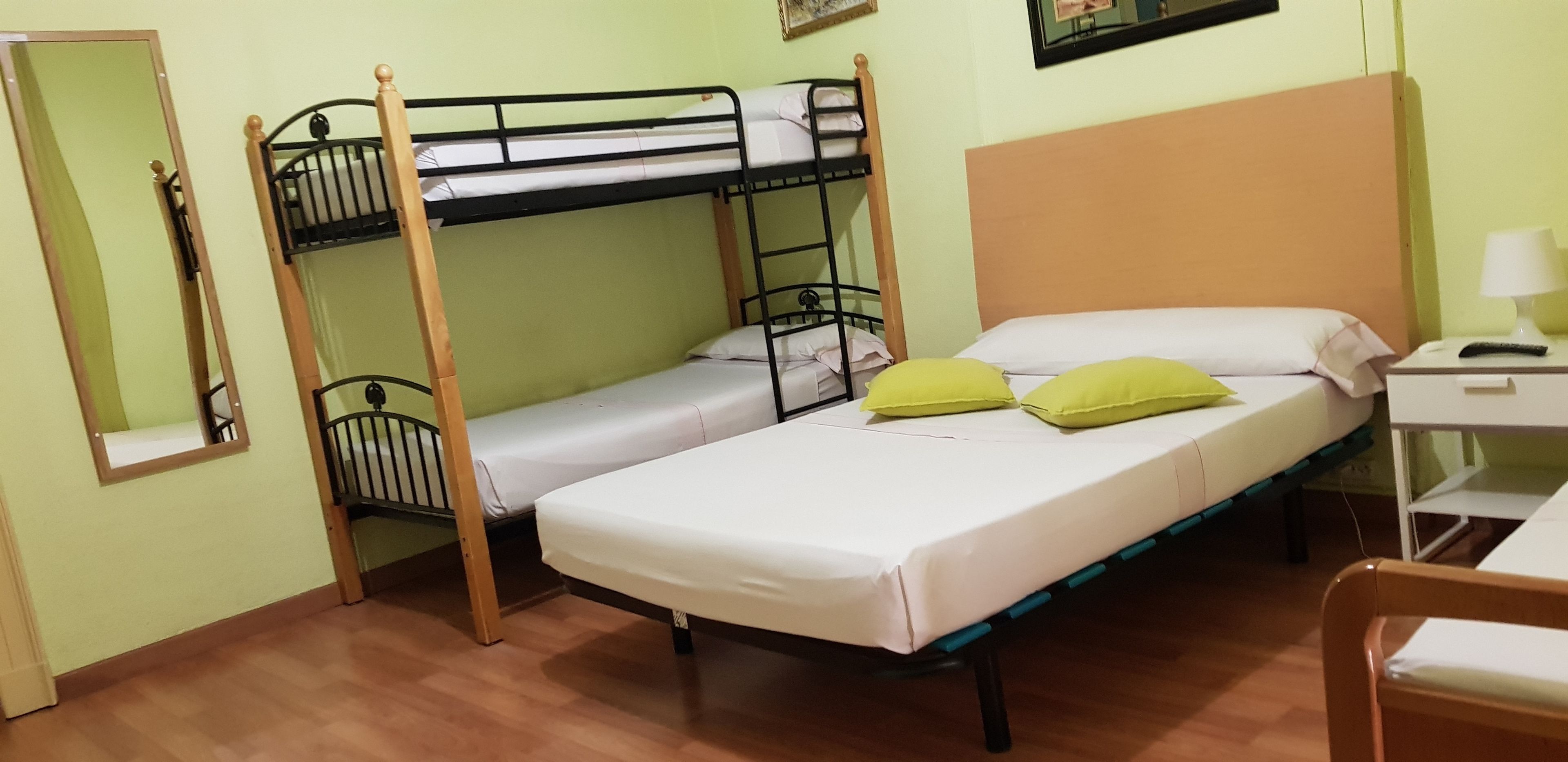 A dormitory room with bunk beds, a desk with a lamp, and a chair.
