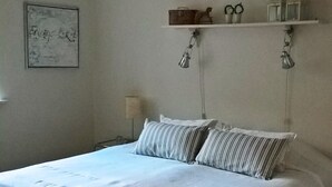 A bedroom with a large bed, wooden flooring, a white wall, a framed picture, and a shelf with decorative items. - Aalborg City apartments (Aalborg)