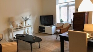 A living room with a TV, a dining table, and chairs. There is a window with a view of the outside. - Aalborg City apartments (Aalborg)