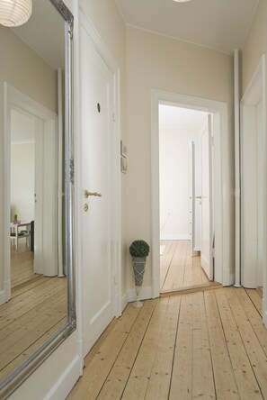 Un couloir doté d’un plancher en bois, de portes blanches et d’un grand miroir.