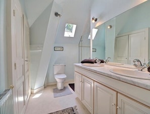 Een badkamer met toilet, twee wastafels, een grote spiegel en een douche.