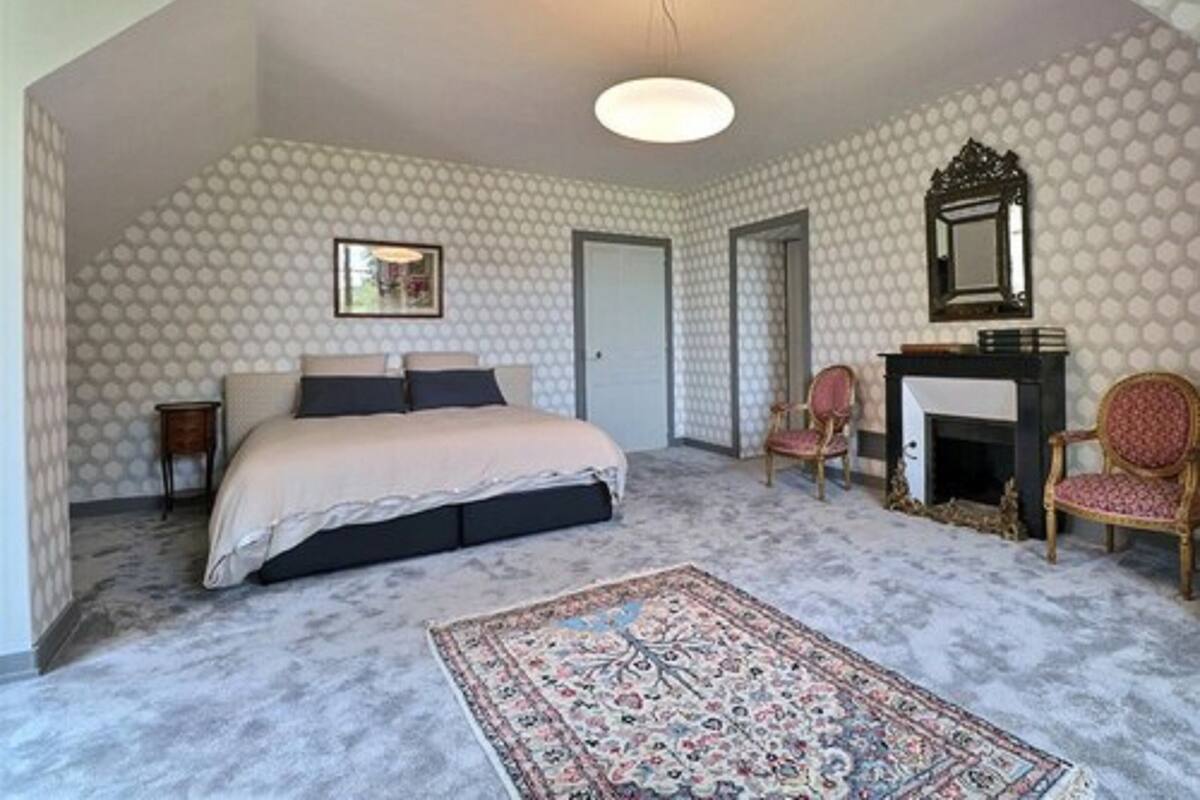 Une chambre à coucher avec un lit, un tapis, une chaise, une cheminée et un papier peint à motifs.