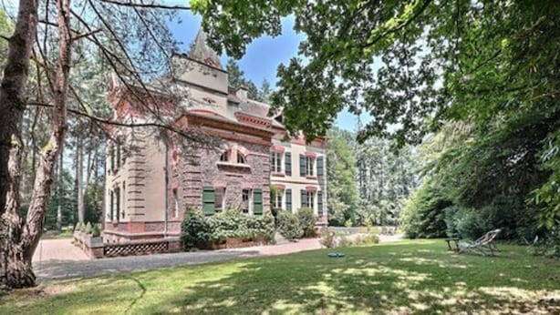 A large stone building with a symmetrical facade, surrounded by lush greenery and trees.