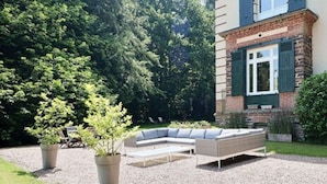 A modern outdoor seating area with a curved bench and a small table, surrounded by a gravel path and potted plants.