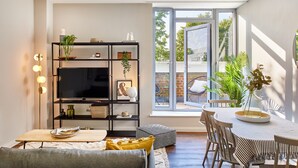 A modern living room with a TV, shelves, and a dining area with a table and chairs. - Designer City Centre Apartment (Coventry)