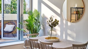 A dining area with a table, chairs, a vase with plants, a mirror, and a view of greenery outside. - Designer City Centre Apartment (Coventry)