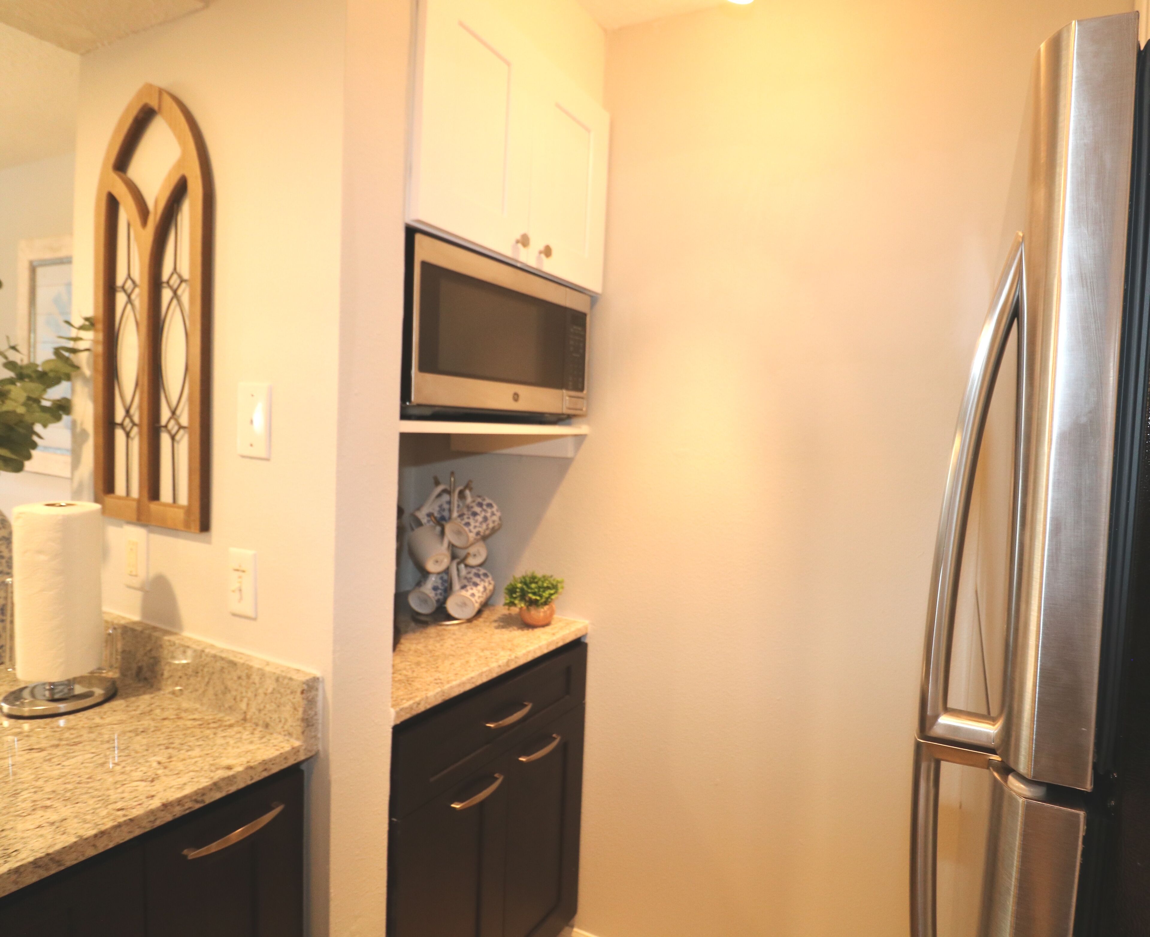 A kitchen with dark cabinets, a stainless steel refrigerator, a microwave, and a countertop with a plant and decorative items.