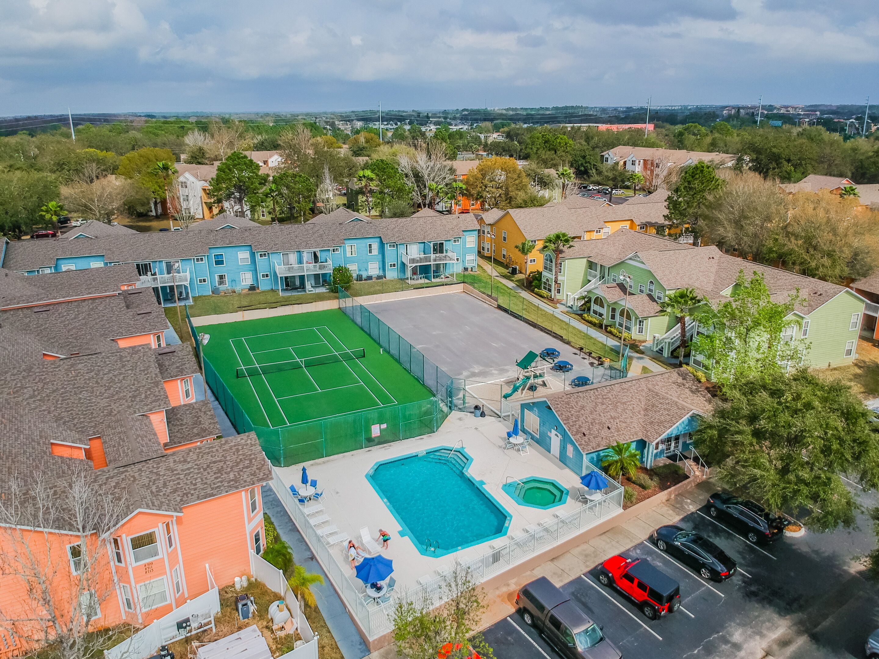 Ovenudblik over et boligområde med farverige huse, en tennisbane og en swimmingpool.