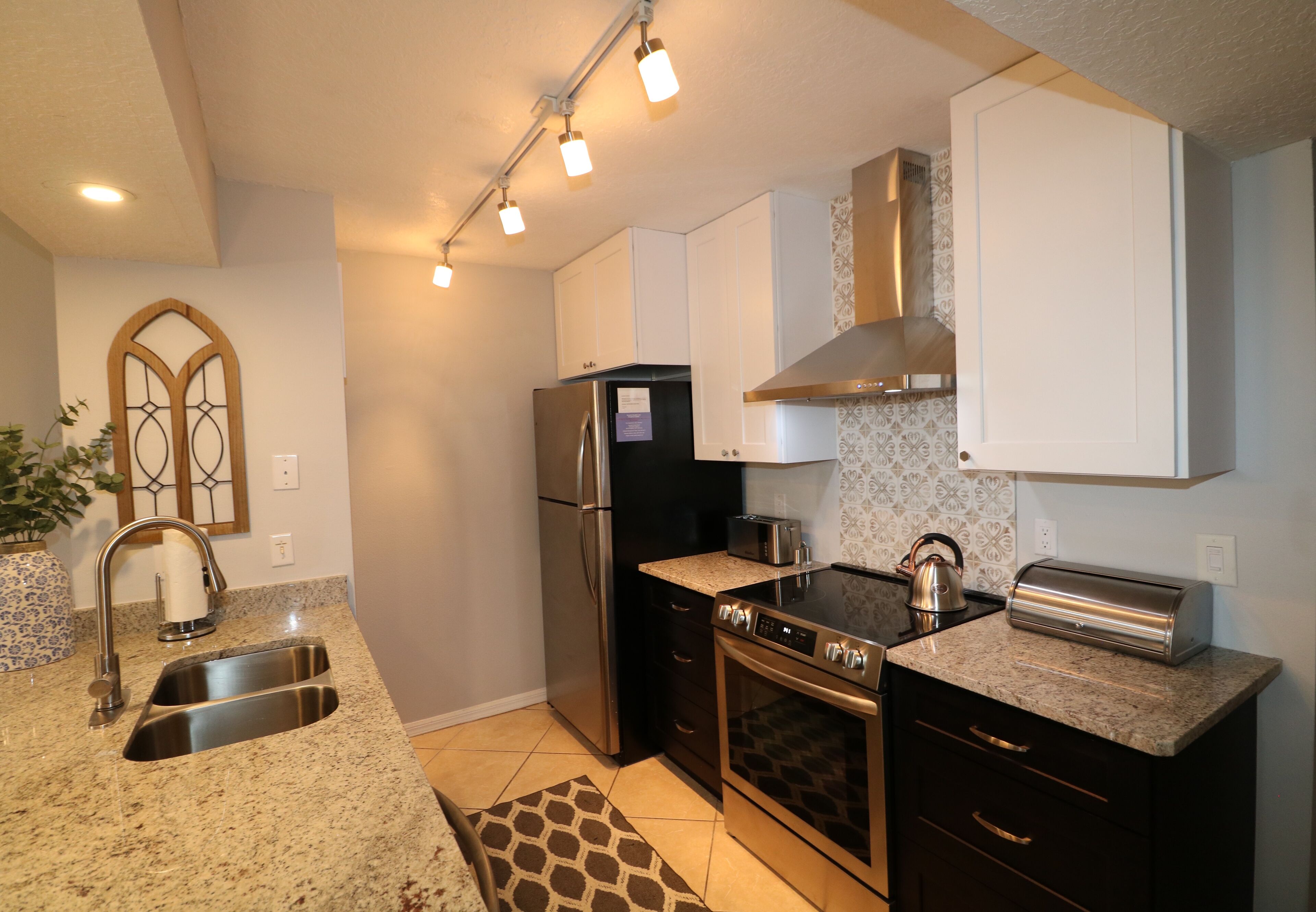 A modern kitchen with stainless steel appliances, a granite countertop, and a patterned backsplash.