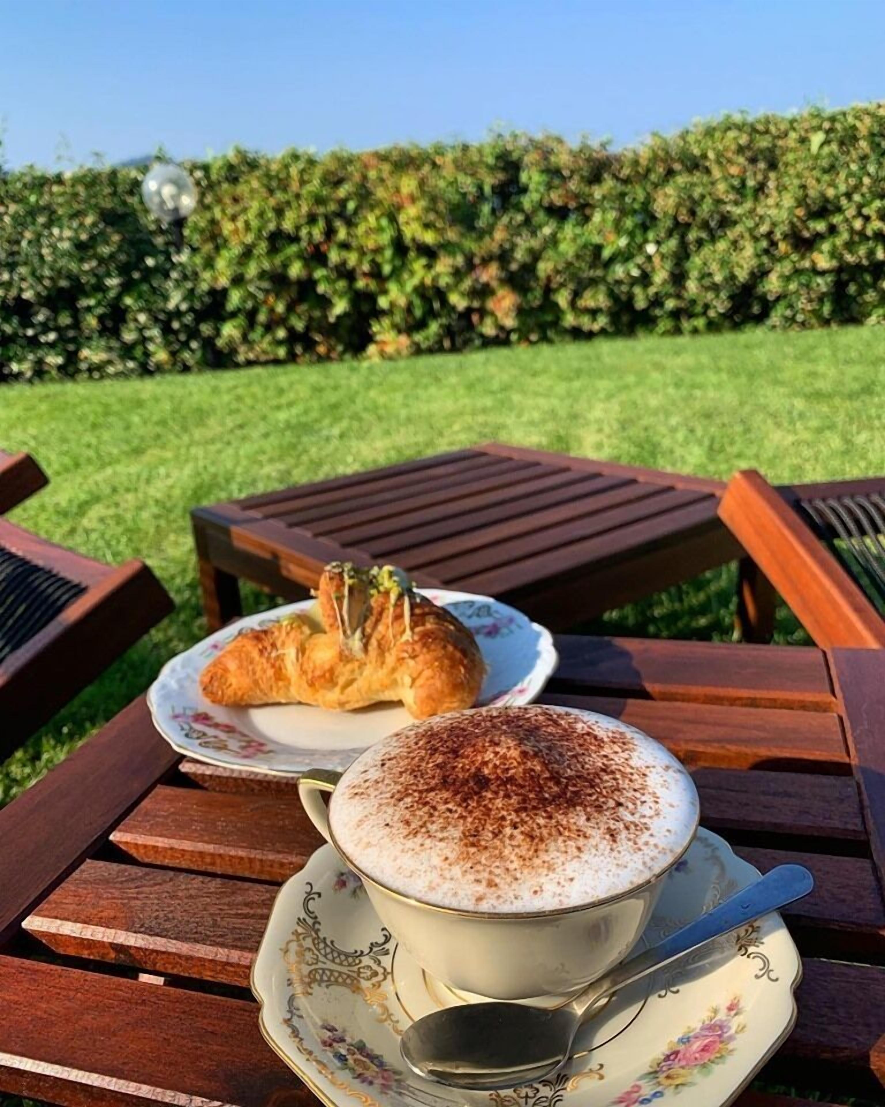 Een tafel met een kop koffie en een croissant op een bord met bloemen.