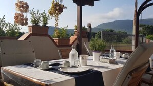 An outdoor dining area with a table set for two, surrounded by chairs, with a view of mountains in the background. - Il Fiore di Loto (San Felice Circeo)