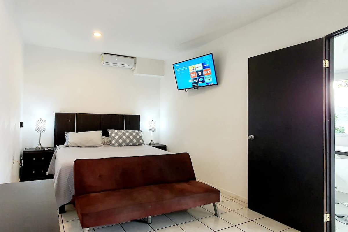 Ein modernes Hotelzimmer mit Bett, einer Couch, einem an der Wand befestigten Fernseher und einer Tür zu einem Balkon.