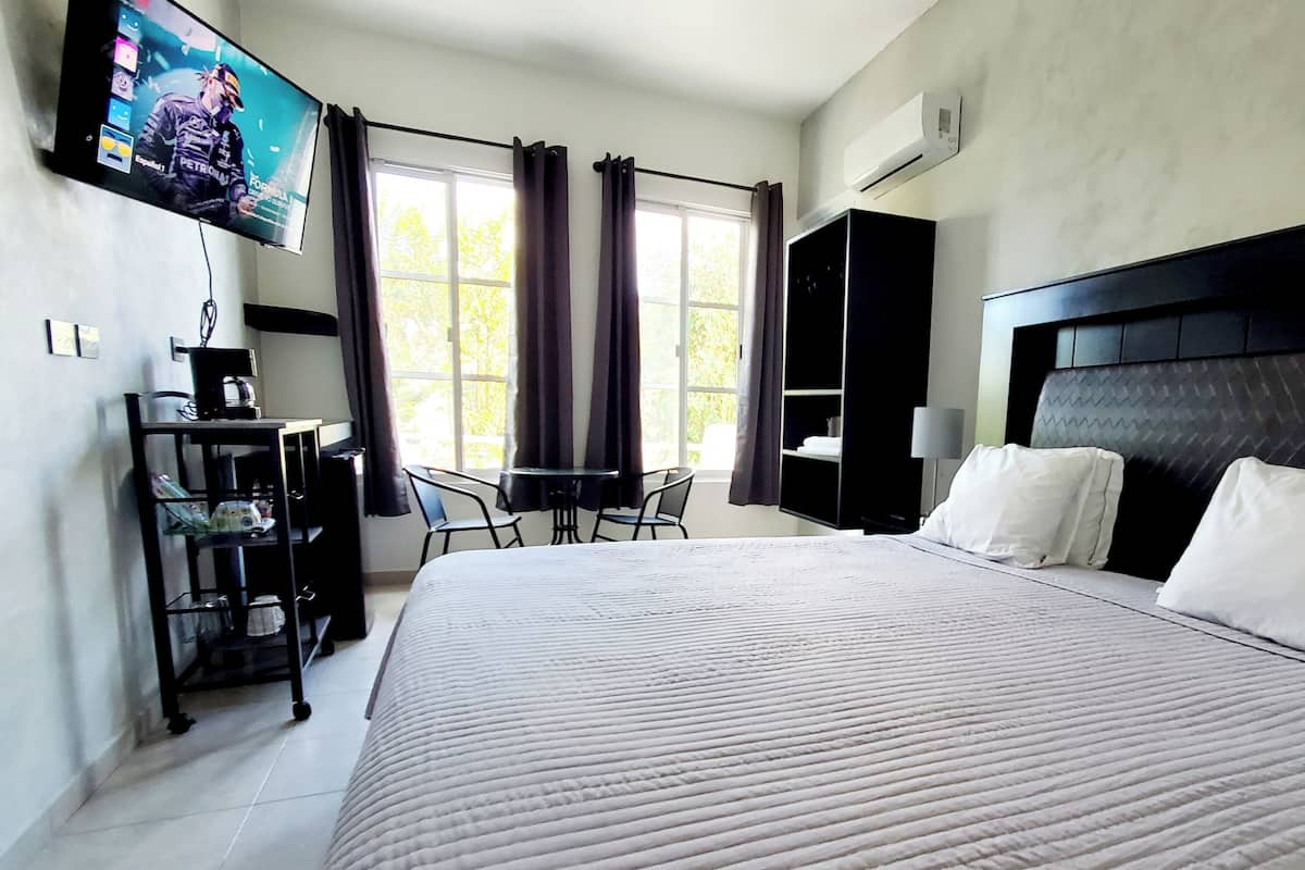 Ein Hotelzimmer mit einem großen Bett, einem an der Wand montierten Fernseher, einem Schreibtisch mit Stuhl und einem Fenster mit Vorhängen.